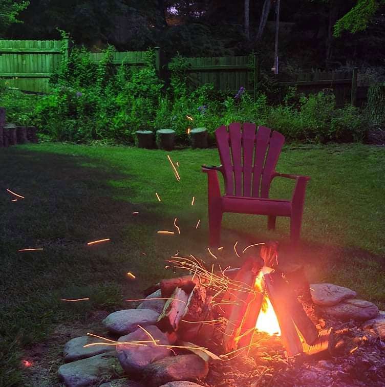 Fire pit burning at night beside an Adirondack chair